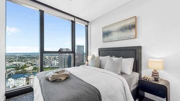 A hotel room with a large window, a bed, a nightstand, and a painting on the wall.