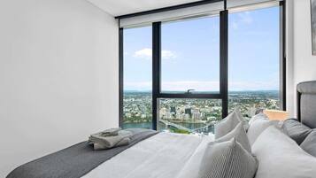 A bedroom with a large window, a bed with pillows, and a view of a cityscape.