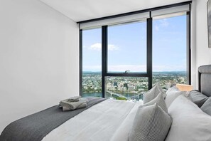 A bedroom with a large window, a bed with pillows, and a view of a cityscape. - Skyrise Style! 1bed/1bath/1car/views! ~ CBD (Brisbane)