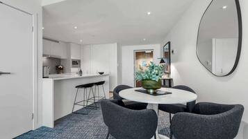 A modern kitchen with white cabinets, a dining area with a round table and grey chairs, and a large mirror on the wall.