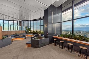 A modern lounge area with seating, a bar, and large windows offering city views. - Skyrise Style! 1bed/1bath/1car/views! ~ CBD (Brisbane)