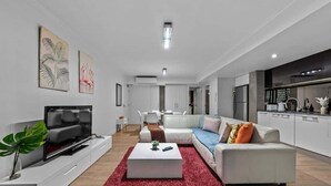 Un salón moderno con un televisor de pantalla plana, sofás blancos, una alfombra roja y obras de arte en las paredes.