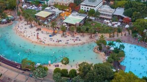 Vista aérea de una zona costera con playa, piscina y edificios circundantes.