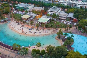 Luftaufnahme einer Küstenlandschaft mit Strand, Pool und umliegenden Gebäuden.