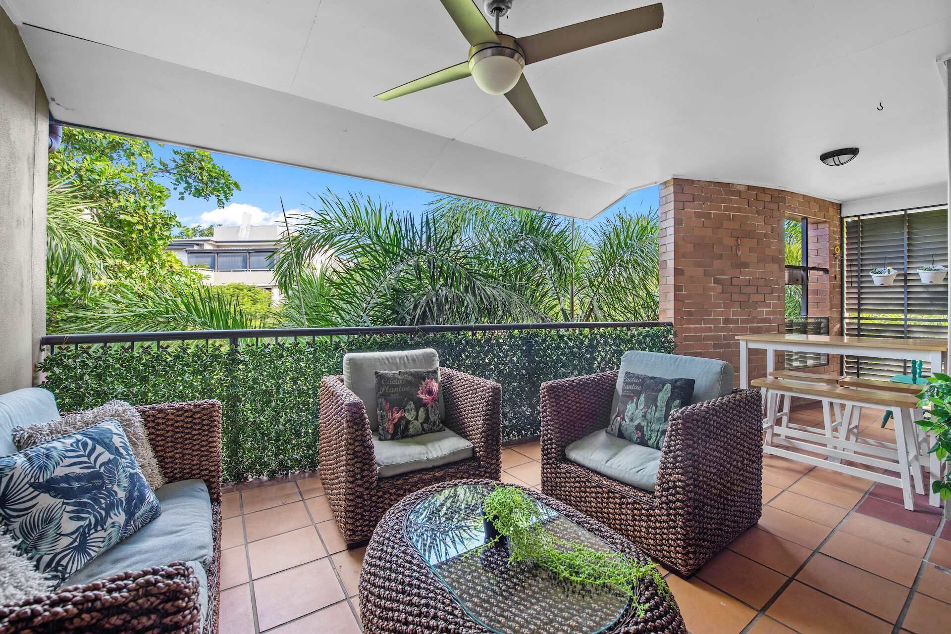 A balcony with wicker furniture, a ceiling fan, and a view of greenery.