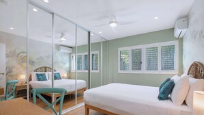 A room with two beds, a dining table, and a chair. There is a window with blinds, an air conditioning unit, and a ceiling fan. - The Fishbowl! 1bed/1bath/1car/pool (Brisbane)