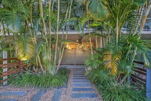 A pathway leading to a building with a glass entrance, surrounded by lush greenery and a wooden fence. - The Fishbowl! 1bed/1bath/1car/pool (Brisbane)