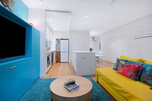 A modern living space with a kitchen, dining area, and a yellow sofa with floral cushions. - The Fishbowl! 1bed/1bath/1car/pool (Brisbane)