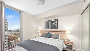 A hotel room with a large bed, two bedside tables with lamps, a view of the city through a large window, and two framed pictures on the wall. - Heart of the CBD ~ 1bed/1bath/balcony/free Parking (Brisbane)