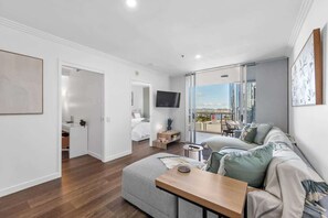 A modern living room with a sofa, a coffee table, and a TV. There is a balcony with a view of the city. - Modern on Mary! 1 Bed,1 Bath,1 Car, Views! (Brisbane)