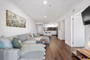 A modern living room with a sofa, a small table, and a kitchen in the background. - Modern on Mary! 1 Bed,1 Bath,1 Car, Views! (Brisbane)