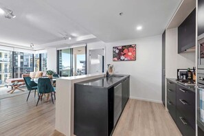 A modern kitchen with a central island, a dining area with chairs, and a large window offering a city view. - South Bank Sensational! ~ 2bed/2bath/1car/pool! (Brisbane)
