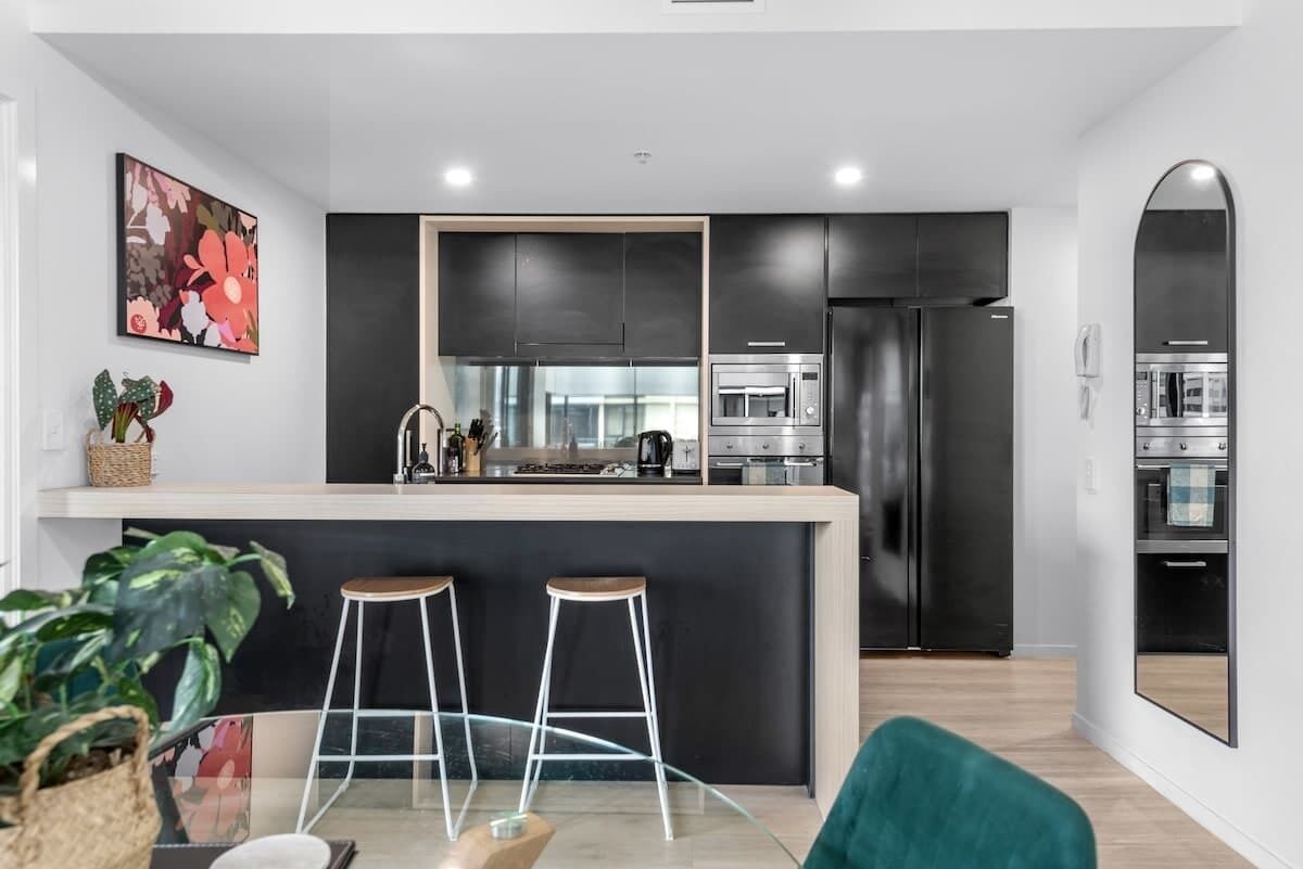 A modern kitchen with dark cabinetry, a central island with stools, and stainless steel appliances.