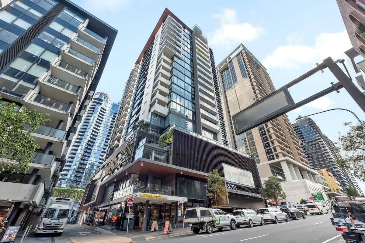 A modern urban street with high-rise buildings, a commercial area with shops, and a busy road with vehicles.