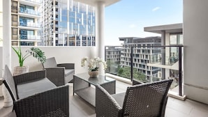 Een balkon met rieten meubels, een glazen tafel en een bloempot.