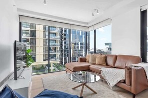 A modern living room with a large window, a leather sofa, a glass coffee table, and a flat-screen TV. - South Bank Sensational! ~ 2bed/2bath/1car/pool! (Brisbane)