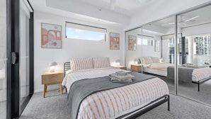 Een moderne slaapkamer met een groot bed, nachtkastjes, een plafondventilator en een grote spiegel.