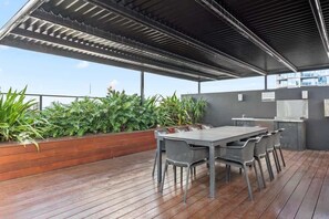 An outdoor patio with a wooden deck, a metal table with chairs, a built-in grill, and a planter with green foliage. - South Bank Sensational! ~ 2bed/2bath/1car/pool! (Brisbane)