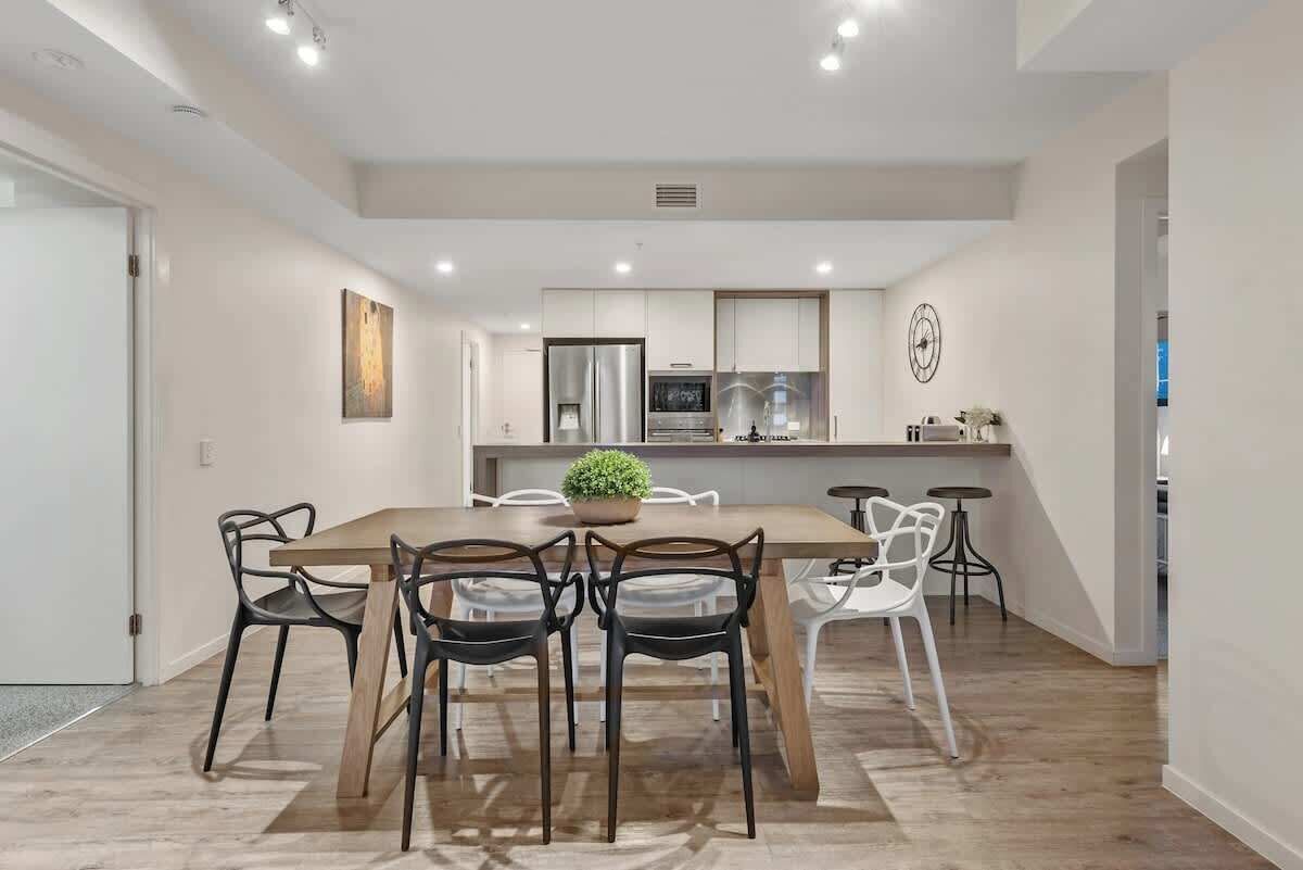 A modern kitchen with white cabinets, a central island with a plant, and a dining area with a wooden table and chairs.