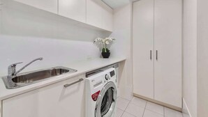 A modern kitchen with a built-in washing machine, a sink, and white cabinetry. - South Bank Stunner! ~ 3 Bed/2 Bath/1car/views (Brisbane)