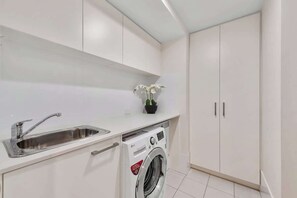 A modern kitchen with a built-in washing machine, a sink, and white cabinetry. - South Bank Stunner! ~ 3 Bed/2 Bath/1car/views (Brisbane)