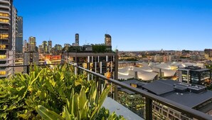 A cityscape with modern buildings, a clear sky, and a balcony with greenery. - South Bank Stunner! ~ 3 Bed/2 Bath/1car/views (Brisbane)