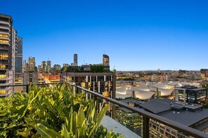A cityscape with modern buildings, a clear sky, and a balcony with greenery. - South Bank Stunner! ~ 3 Bed/2 Bath/1car/views (Brisbane)
