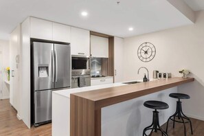 A modern kitchen with a stainless steel refrigerator, built-in oven, and a wooden island with bar stools. - South Bank Stunner! ~ 3 Bed/2 Bath/1car/views (Brisbane)