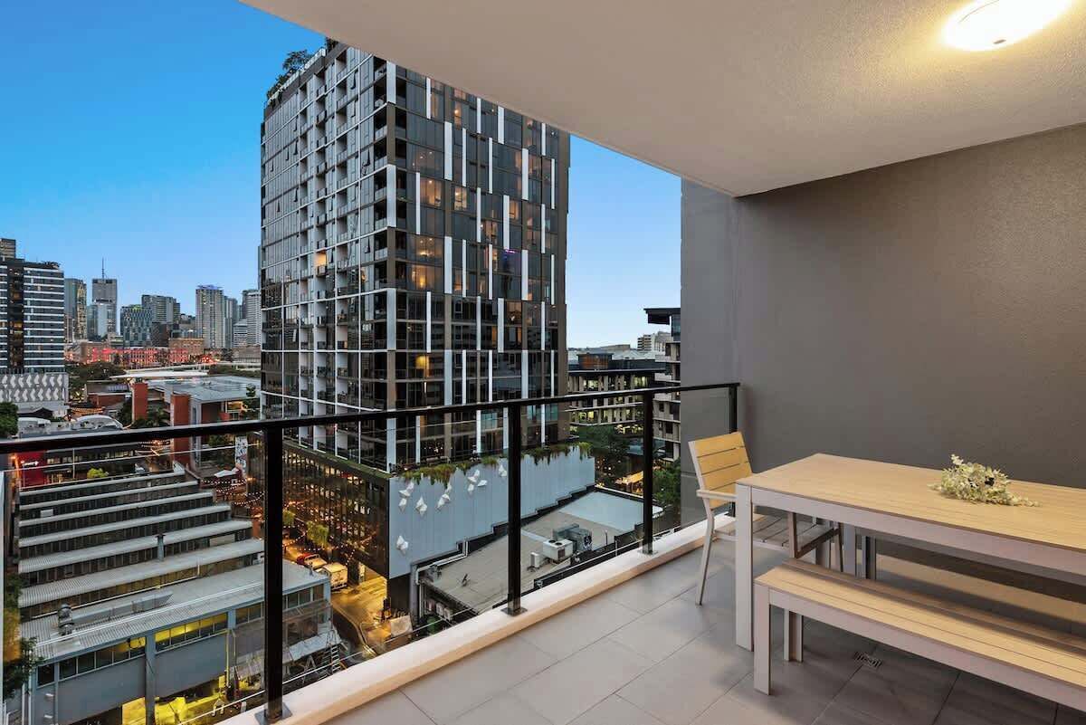 A high-rise building with a modern design, a balcony with a table and chairs, and a cityscape view.
