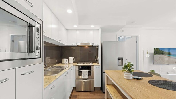 A modern kitchen with stainless steel appliances, white cabinetry, and a wooden countertop. - Urban Retreat 1bed-1bath-study-balcony-1car (Brisbane)