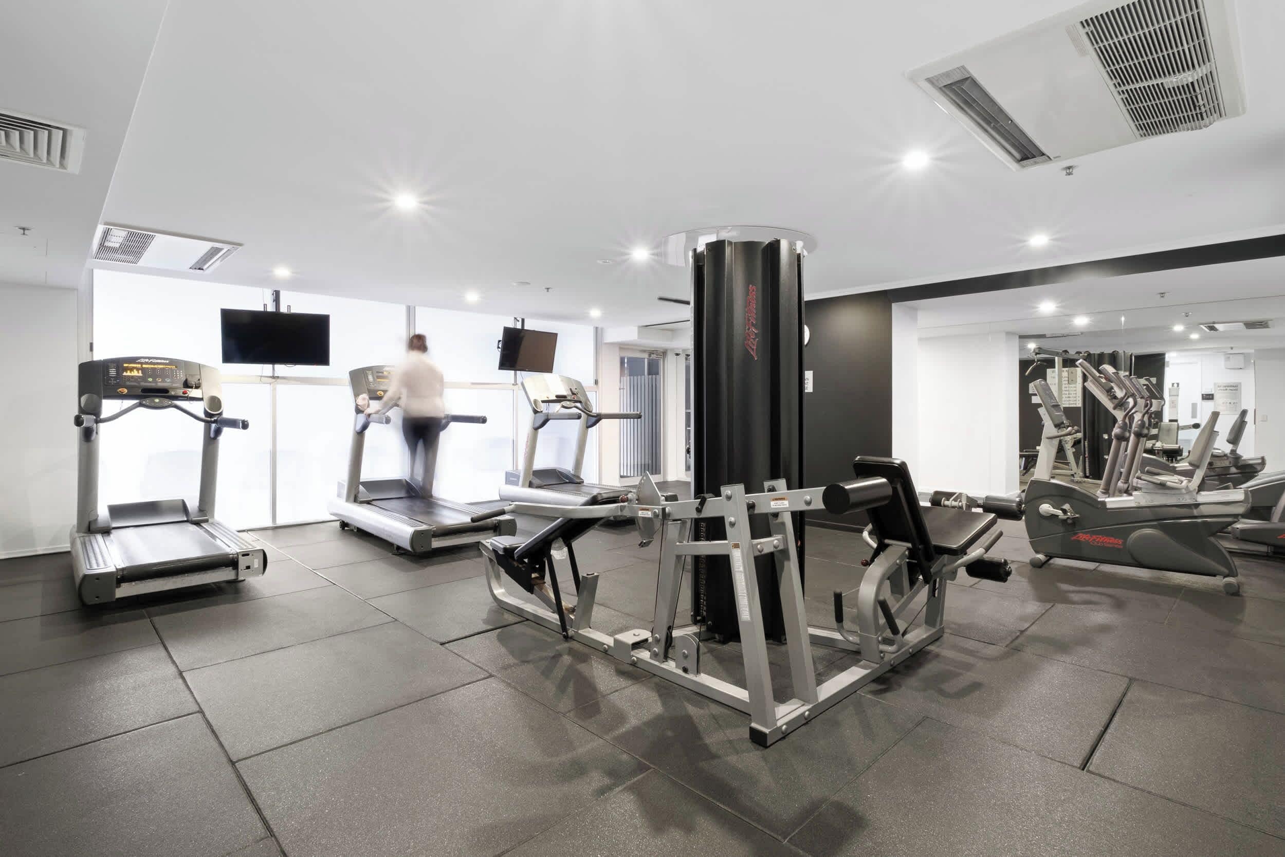 Un gimnasio con cintas de correr, máquinas de pesas y una pantalla de televisión.