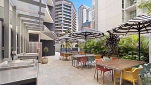 An outdoor patio with tables and chairs, umbrellas, and a staircase leading to an upper level. - Urban Retreat 1bed-1bath-study-balcony-1car (Brisbane)