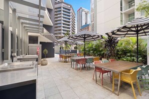 An outdoor patio with tables and chairs, umbrellas, and a staircase leading to an upper level. - Urban Retreat 1bed-1bath-study-balcony-1car (Brisbane)