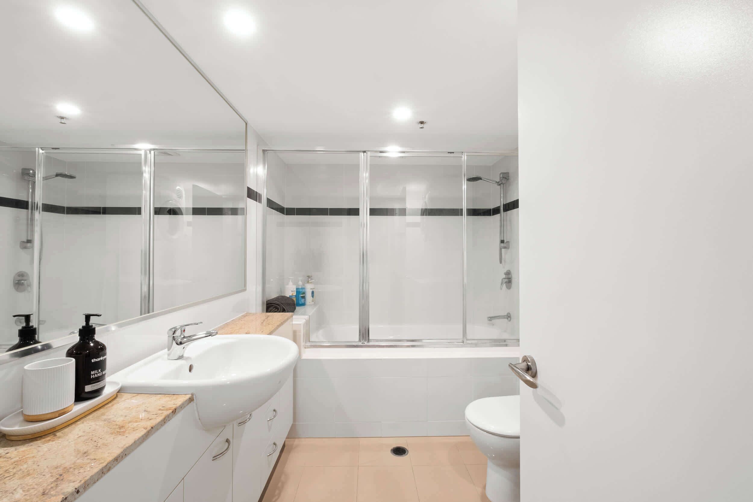 A modern bathroom with a glass-enclosed shower, a white sink, and a toilet.