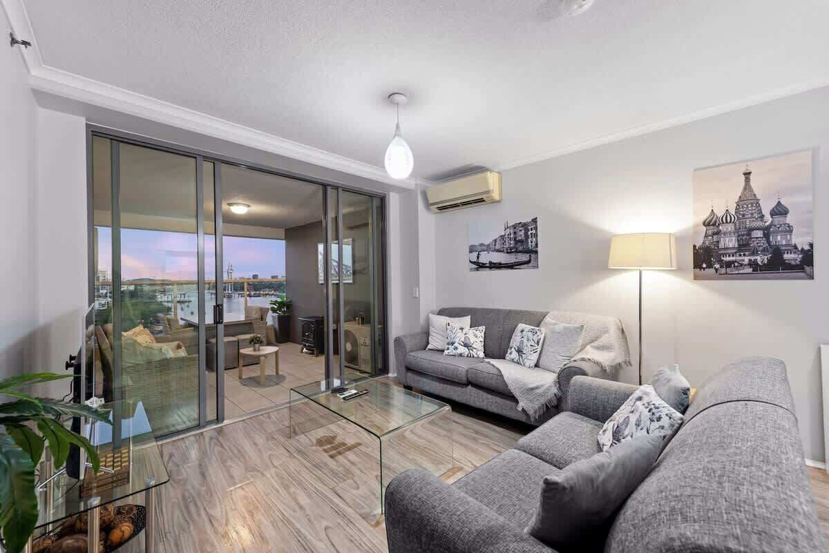 Sala de estar moderna com um sofá cinzento, mesa de centro de vidro e vista para a cidade através de amplas portas deslizantes.