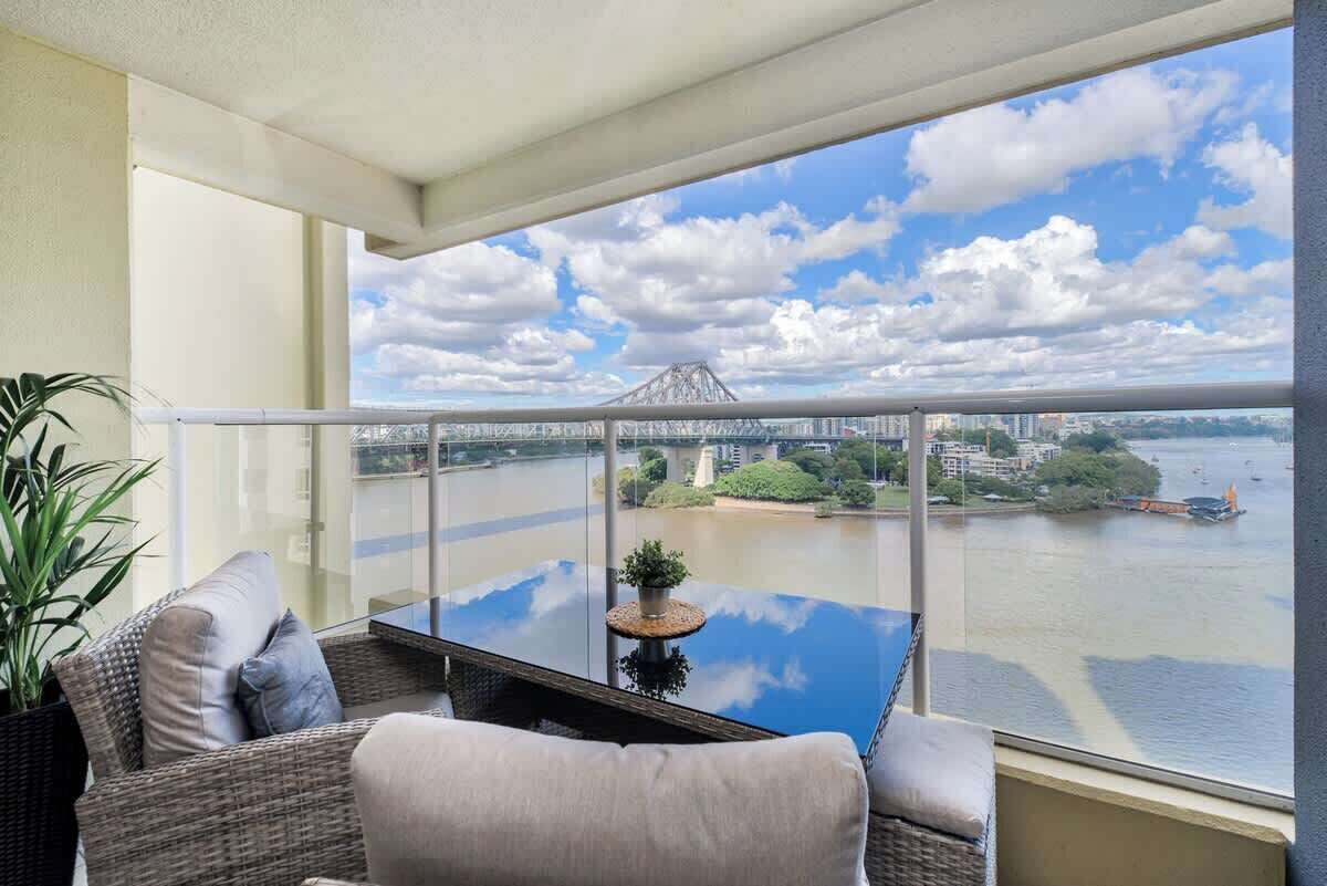 A balcony with a glass table, wicker furniture, and a view of a river and bridge.