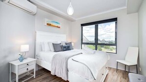 A modern bedroom with a bed, bedside table, lamp, and a window with a city view. - Spectacular! 2bed, 1bath, 1car, Views ~ CBD (Brisbane)