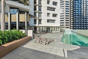 Ein Poolbereich auf dem Dach mit Liegestühlen, einem Pool und einem mehrstöckigen Gebäude im Hintergrund.
