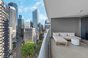 Ein Balkon mit einer Couch und Hocker, mit Blick auf eine Skyline moderner Gebäude.