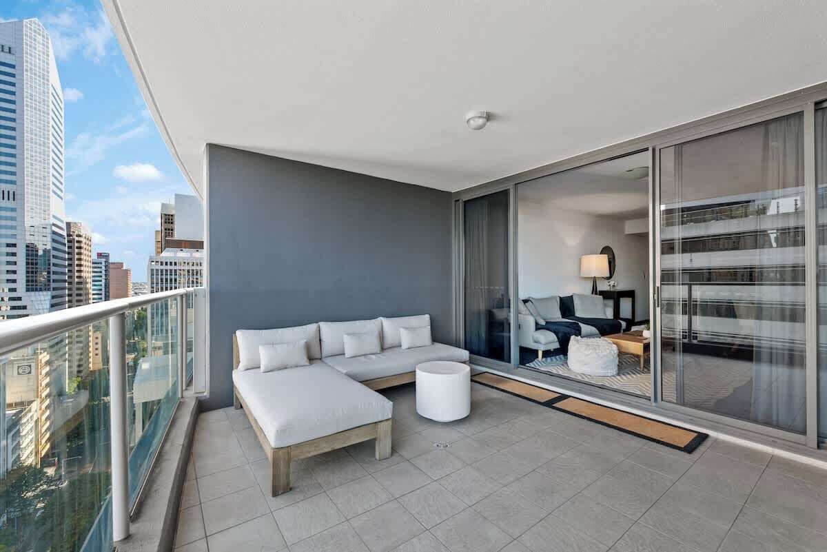A modern balcony with a sofa, a small table, and a view of the cityscape.