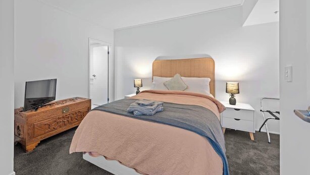 A bedroom with a bed, a wooden dresser, a television, and a nightstand with lamps. - Top of the Town! 2bed/2bath/1car/balcony/views~cbd (Brisbane)