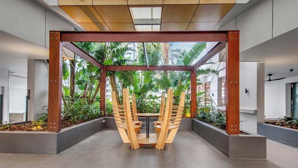 Ein modernes Interieur mit einer zentralen Holzkonstruktion, möglicherweise eine Sitzgruppe, umgeben von einem Betonboden und Metallträgern.