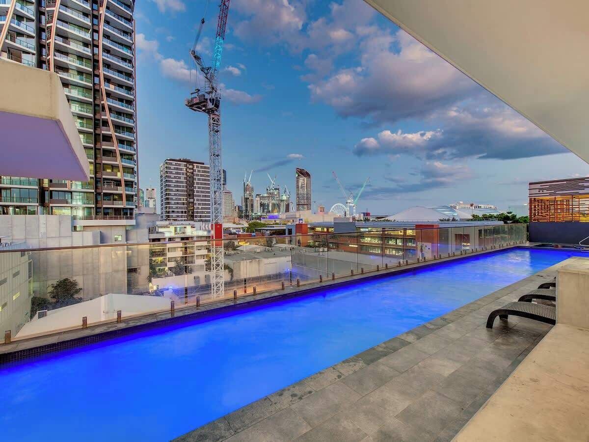 Une piscine sur le toit offrant une vue panoramique sur la ville, avec ses gratte-ciel et ses grues de construction.