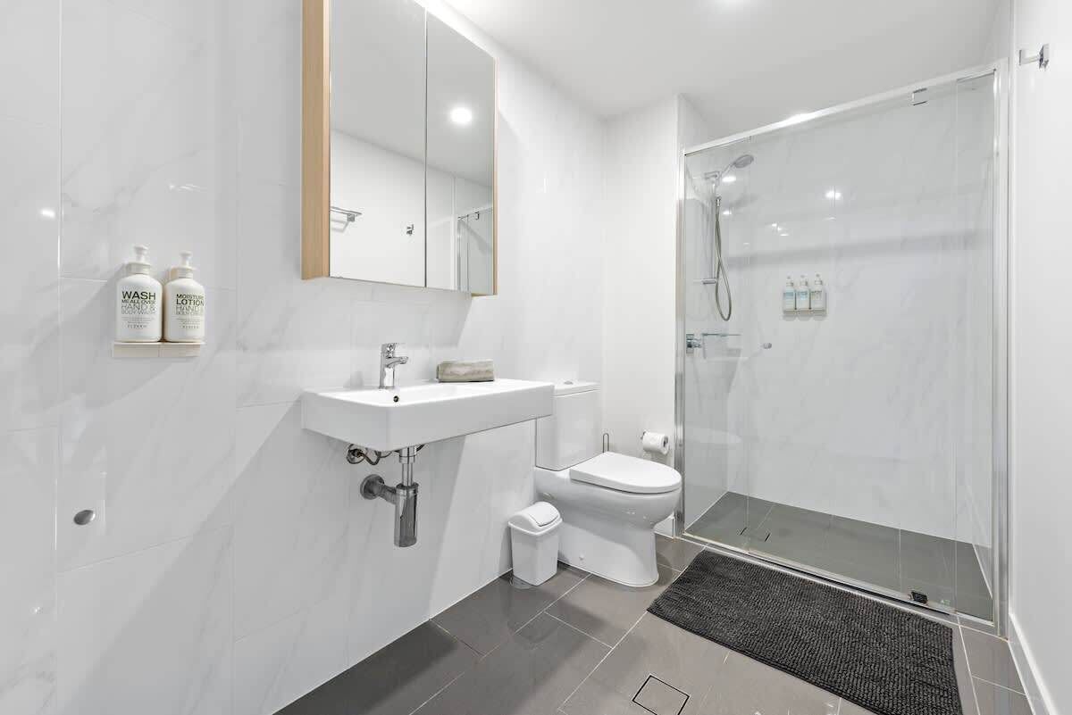 A modern bathroom with a white sink, toilet, and glass shower enclosure.