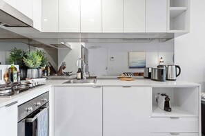 A modern kitchen with white cabinetry, a built-in oven, a sink, and a coffee maker. - Resort-style Living! ~ 1bed/1bath/1car (Brisbane)