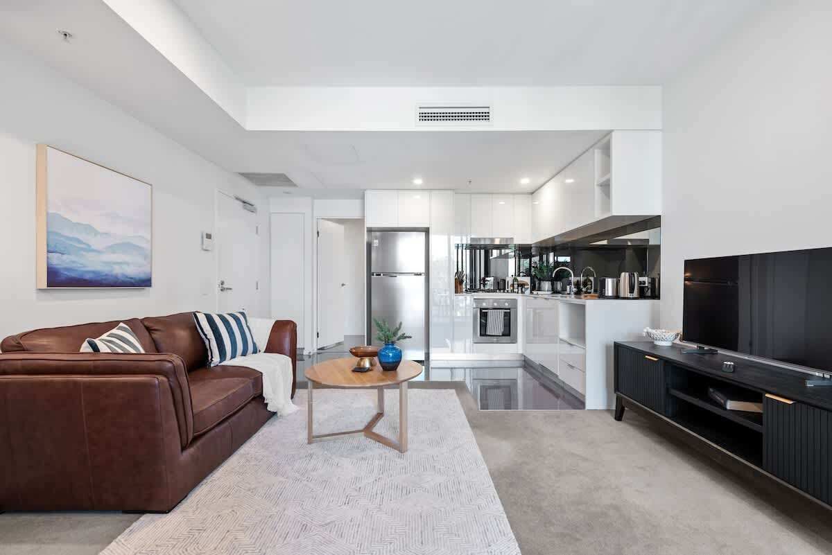 A modern living room with a brown leather sofa, a small round table, and a flat-screen TV.