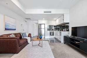 A modern living room with a brown leather sofa, a small round table, and a flat-screen TV. - Resort-style Living! ~ 1bed/1bath/1car (Brisbane)