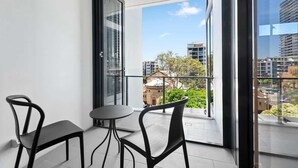 Ein Balkon mit zwei Stühlen, einem Tisch und einer Glastür, mit Blick auf Gebäude und Grünflächen.