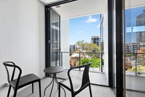 A balcony with two chairs and a table, a glass door, and a view of buildings and greenery. - Resort-style Living! ~ 1bed/1bath/1car (Brisbane)