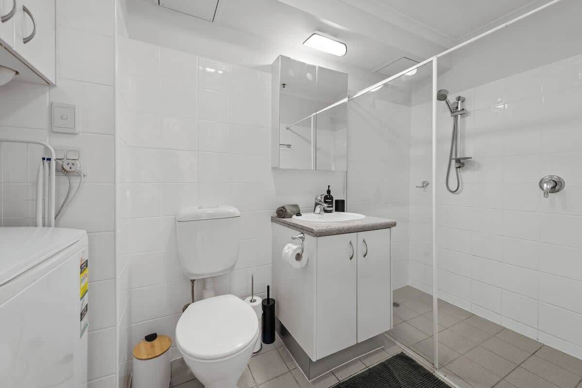 Ein modernes Badezimmer mit Toilette, Waschbecken, Spiegel, Dusche und gefliesten Wänden.